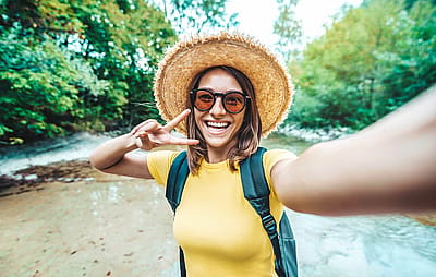 Happy female tourist with backpack taking selfie picture with smart mobile phone outside - Millenial woman having fun on adventure trip - Traveling and technology concept