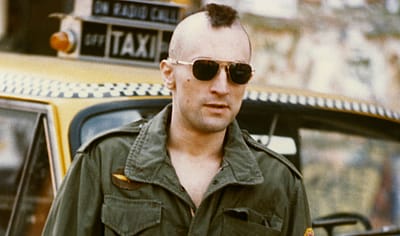 Robert De Niro, as Travis Bickle in the 1976 Martin Scorsese film 'Taxi Driver', with his iconic Mohawk haircut standing by a New York Yellow Taxi Cab.