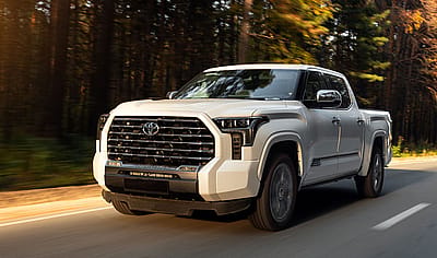 White Toyota Tundra pickup truck driving on a forest road at golden hour