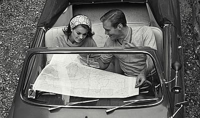 A black and white photo of a couple on reading a map on a road trip.