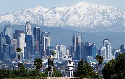 People take in the view of the downtown skyline with the snow-capped San Gabriel Mountains visible beyond on February 23, 2026 in Los Angeles, California.