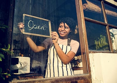 A woman holding an open sign in the window of a business.