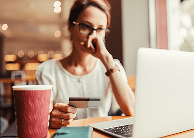 A woman holds a credit card and looks at her laptop with concern.