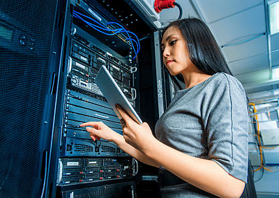A young tech engineer working with a tablet in a network server room.