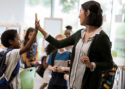 An elementary school teacher high fives a student.