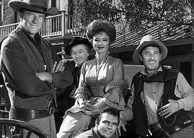 The cast of 'Gunsmoke' poses around a wagon in a promotional portrait for the Western television series. From left to right are actors James Arness, Milburn Stone, Amanda Blake, Ken Curtis, and Burt Reynholds is on the second row.