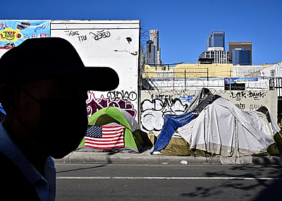 A man walking in front of a homeless encampment.
