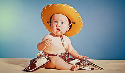 960s Baby Boy With Surprised Facial Expression Dressed As Cowboy Wearing Hat And Holster And Gun