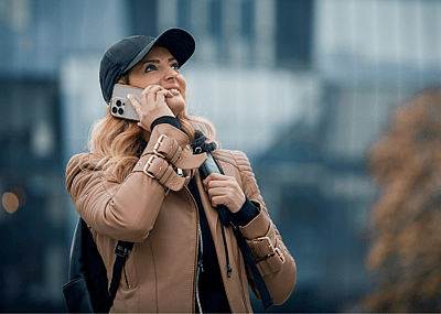 A woman in a black baseball hat and cream jacket holding a cellphone to her ear and looking up.
