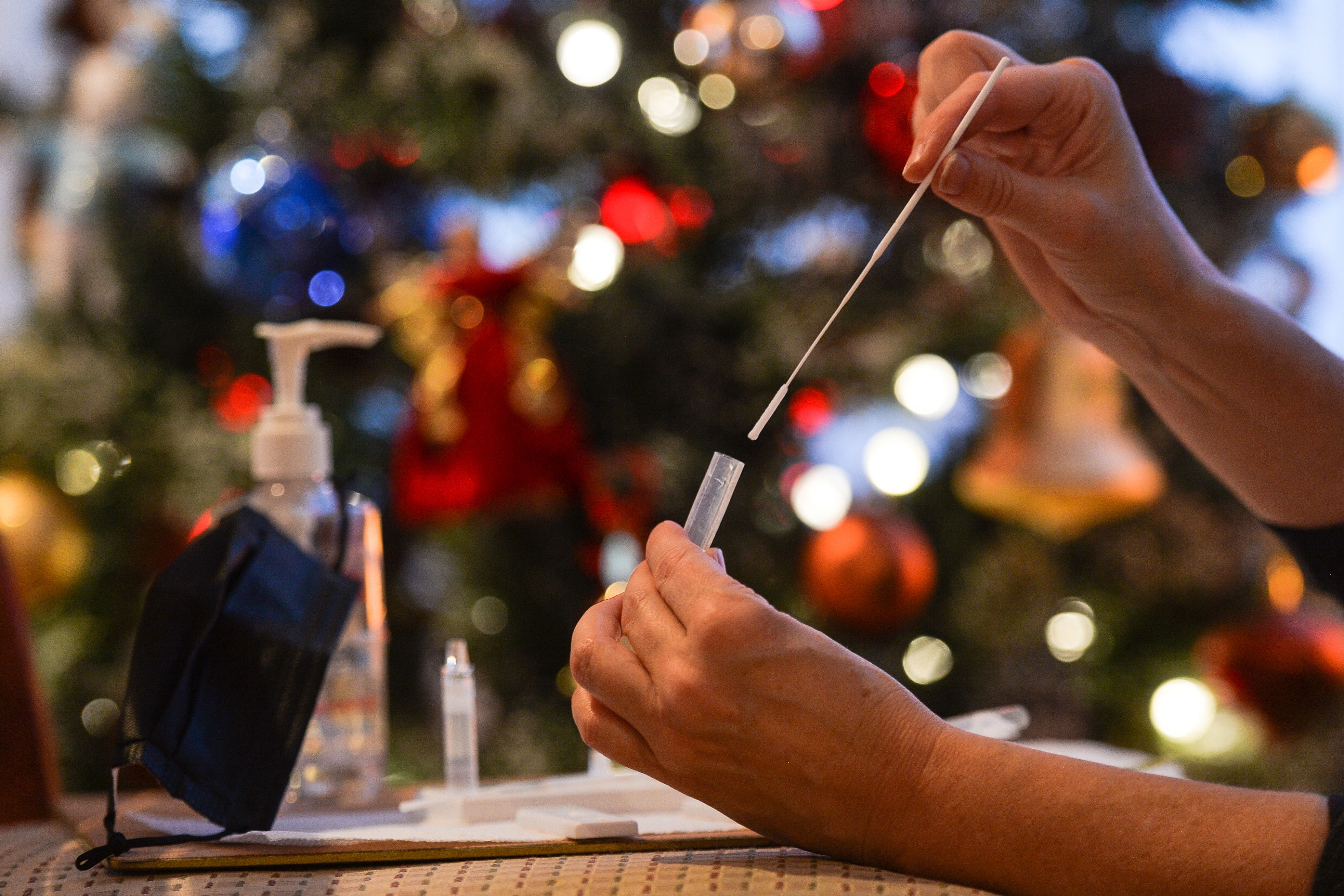 A person uses a COVID test with a Christmas tree in the background.