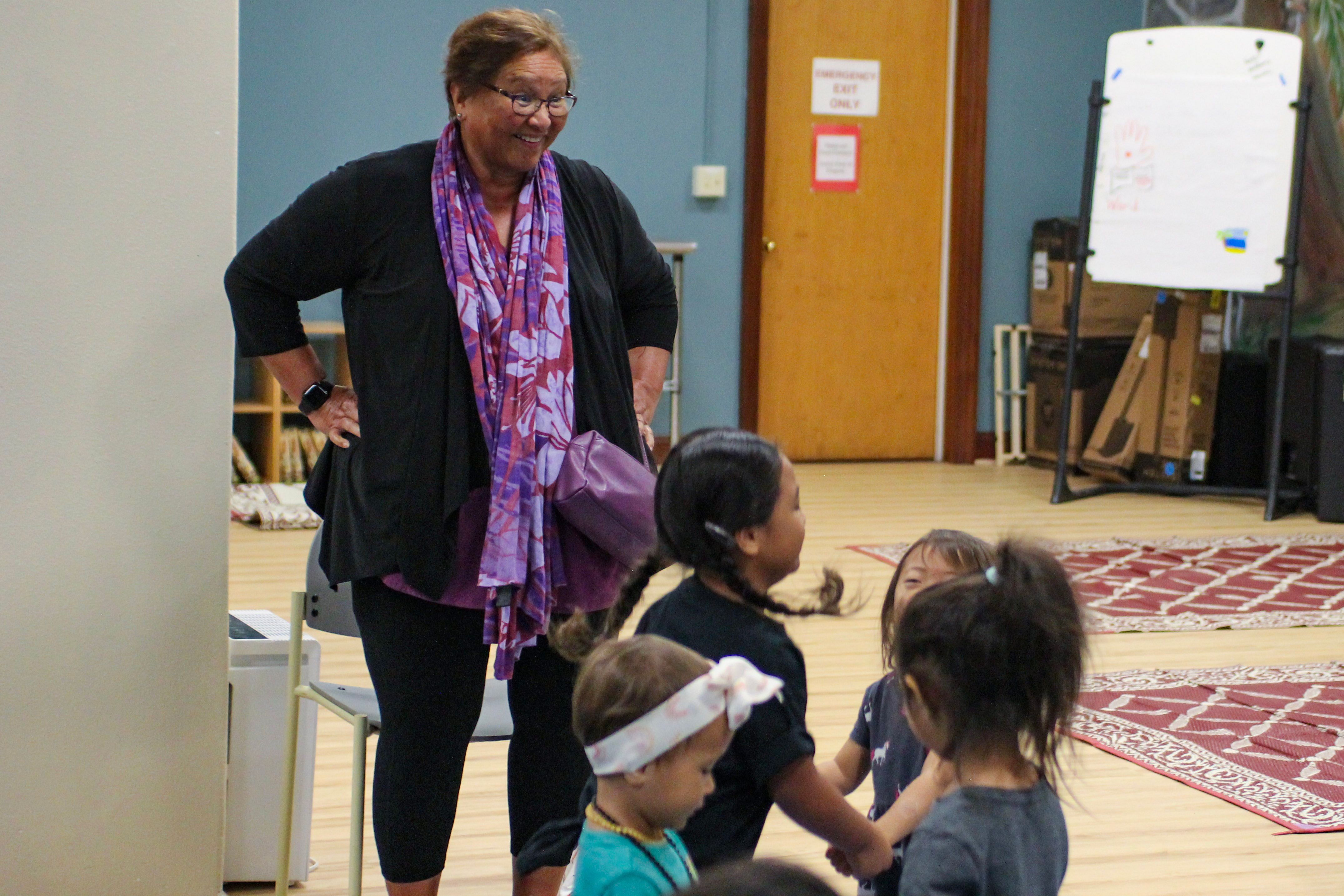 A woman smiles while watching several children interact.