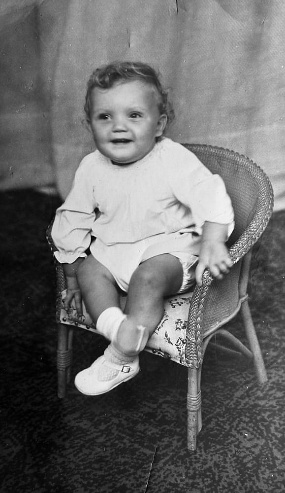 Black and White photo of a child sitting in a chair, smiling at the camera.