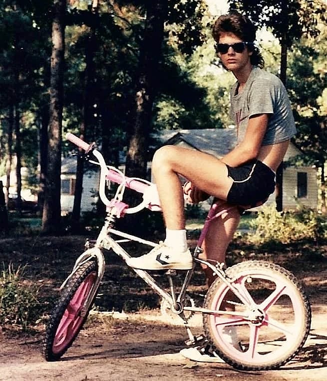 Kid with a mullet sitting on a BMX bike