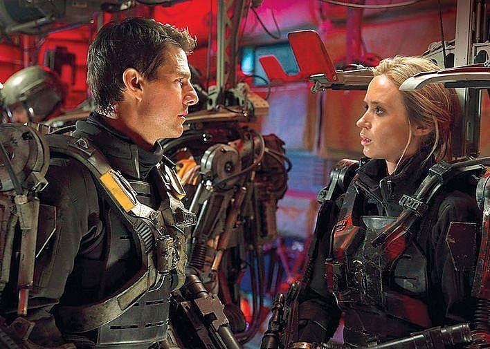Tom Cruise and Emily Blunt, dressed in dark armor, look seriously at each other.