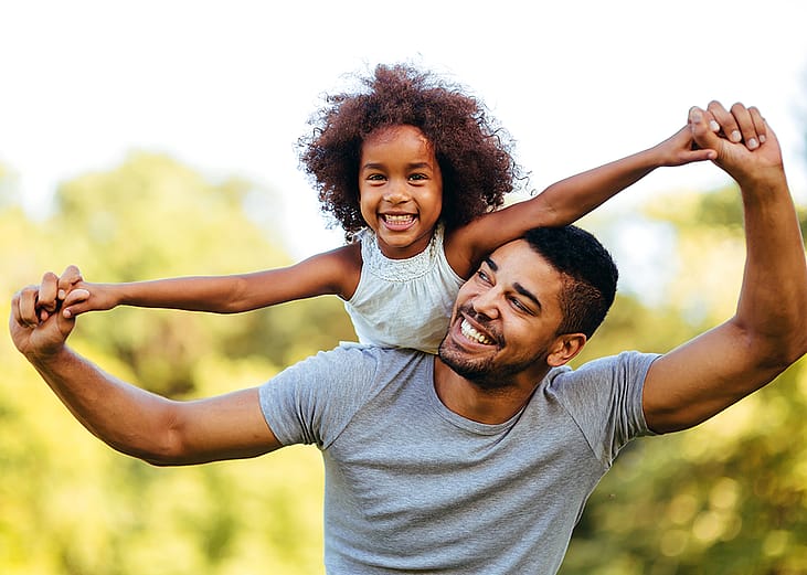Father carrying daughter on shoulders in park.