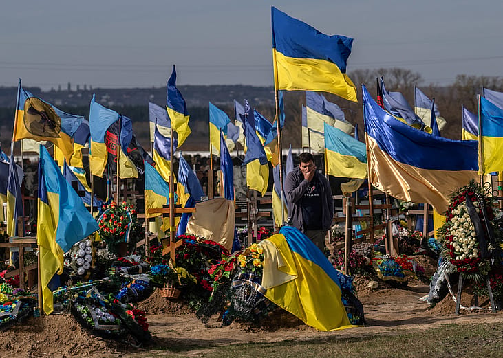 A man pauses by a grave as Ukrainian flags fly in a cemetery for soldiers killed in action.