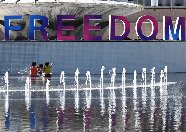 Children play in a fountain near a sign reading “Freedom”