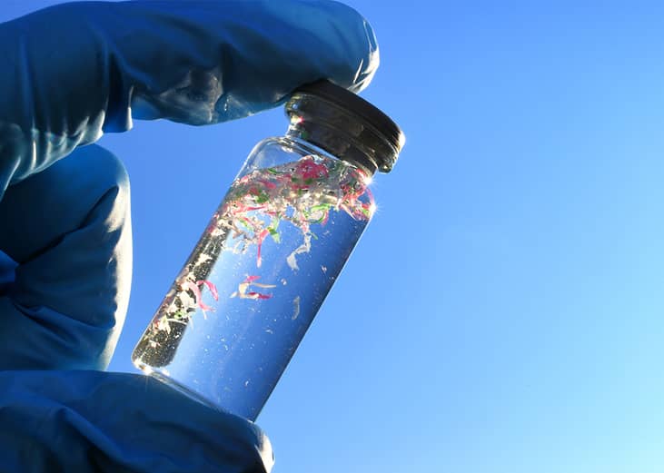 Glass vial with water samples contaminated with microplastics against blue sky.
