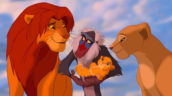 A monkey holding a lion cub in between the mother and father lions.