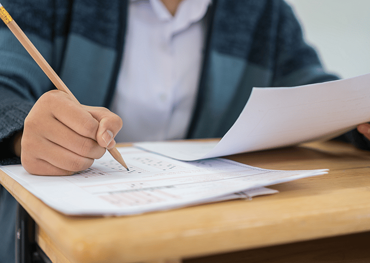 Closeup of student taking an exam at a desk, filling in an answer sheet with a pencil.