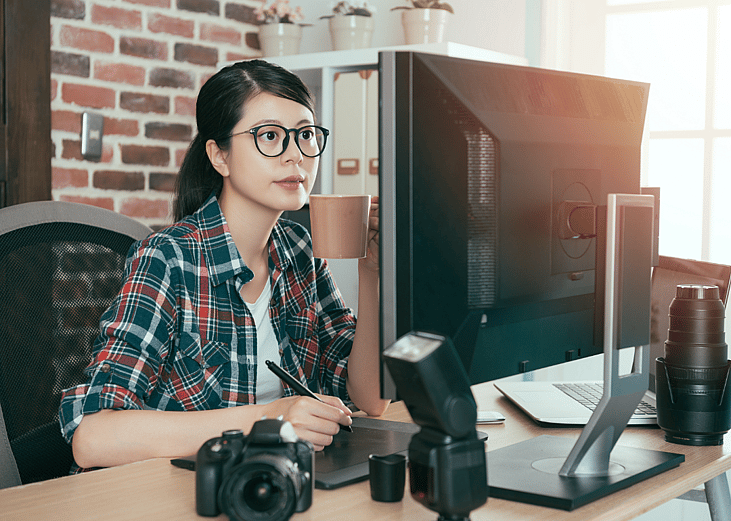 A woman with glasses looks intently at her monitor with camera equipment around her. 
