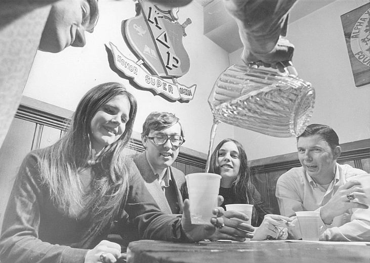 College students sitting at a table enjoying a pitcher of beer.
