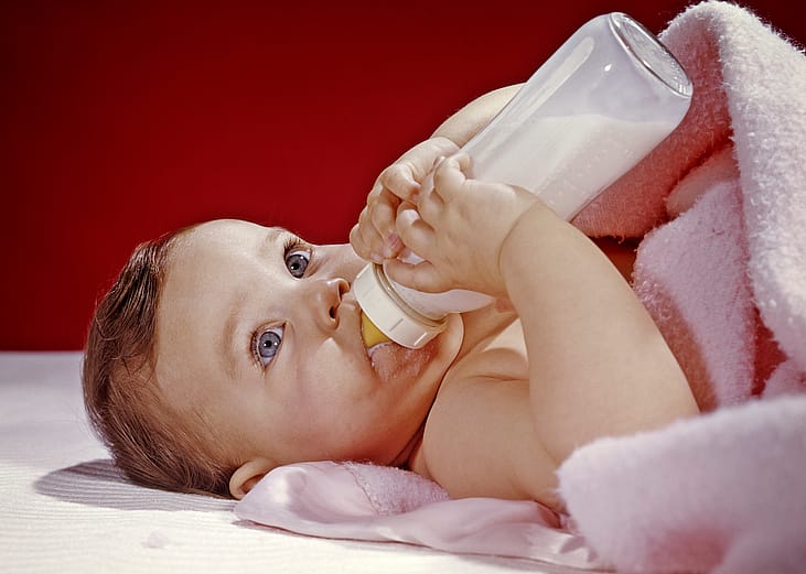 Baby in the 1960s holding a bottle while wrapped in a pink blanket.