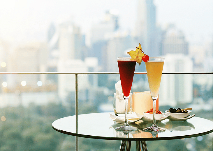 Two cocktails on a table on a rooftop bar in a city.