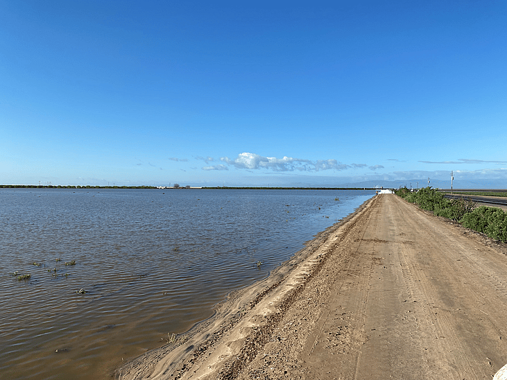 A flooded farm with a dirt road running alongside it