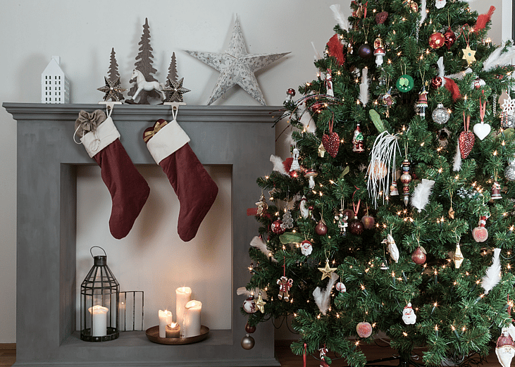 A Christmas tree stands beside a fireplace decorated with stockings
