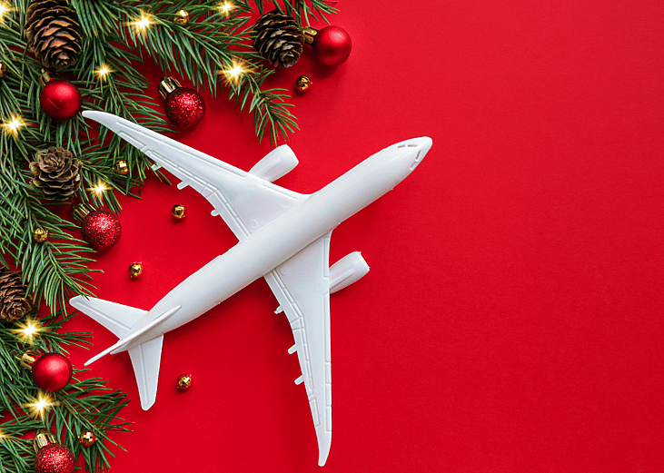 A conceptual image of a white airplane model against a red background with holiday foliage