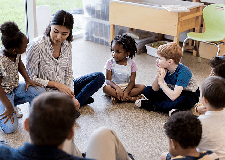 elementary school students sitting in a circle talking to teacher