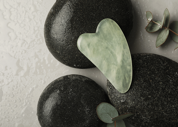 jade color gua sha tool displayed on black stones