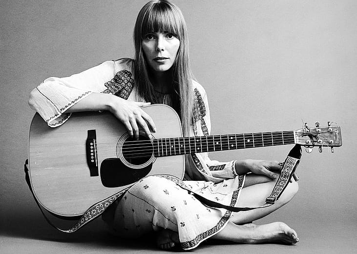 Portrait of musician Joni Mitchell seated on the floor with her acoustic guitar in her lap in 1968.