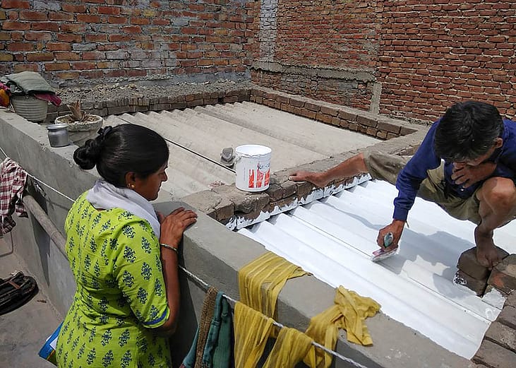 Residents of an informal settlement in India’s Ahmedabad city work on painting their home with sun-reflective white paint