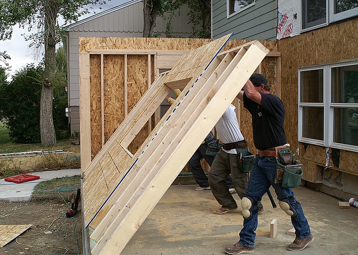 two people raising the plywood frame where a wall will go up during a home addition