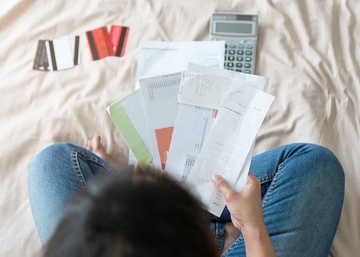A person holding bills and receipts with credit cards and a calculator nearby.