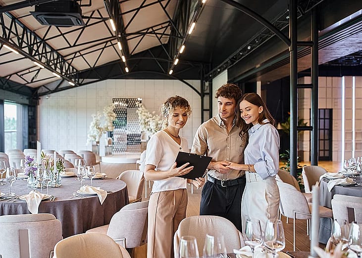A couple engaging in a discussion with a wedding coordinator inside a wedding venue.