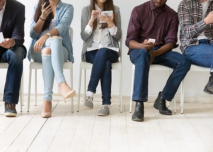 A group of five students sitting in a waiting room, all using their devices.