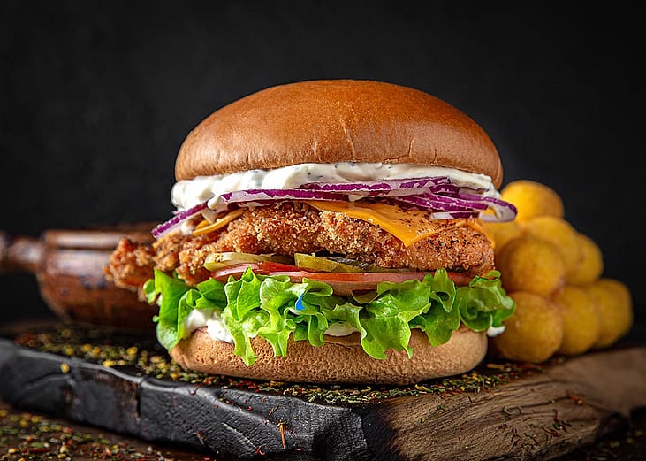 A close-up of a burger sitting on wooden cutting board against a black background.