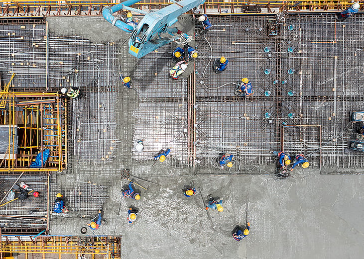 An aerial view of construction workers pouring concrete for a project site.