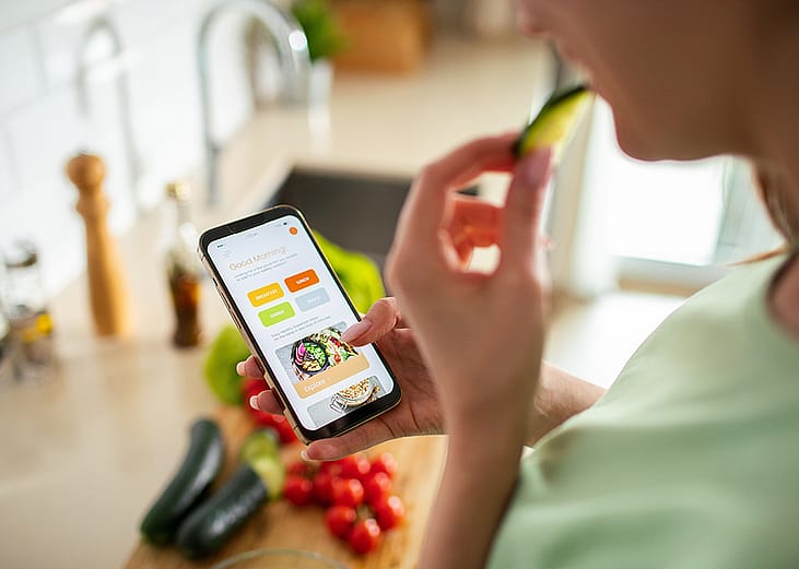 A woman is looking up meal plans on her phone while preparing food.