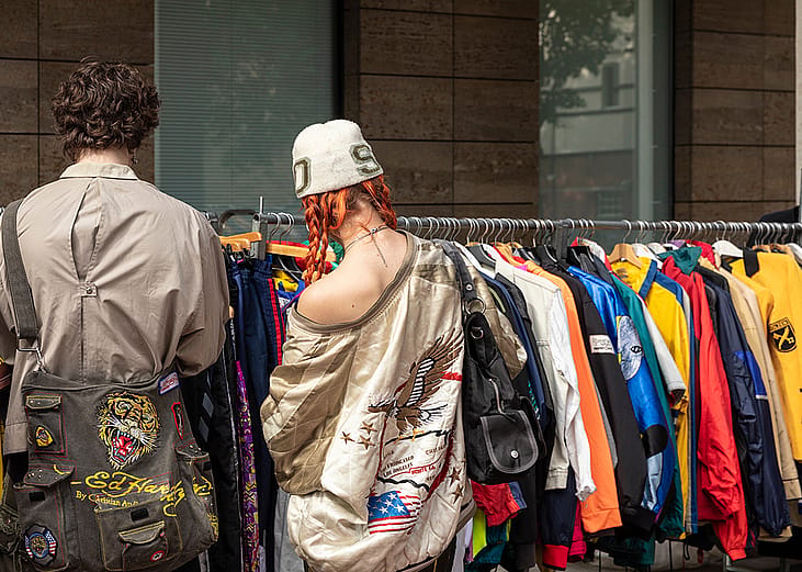 Two people browsing through vintage jackets at a thrift stand.