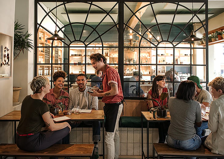 A waiter taking orders from customers in a busy restaurant.
