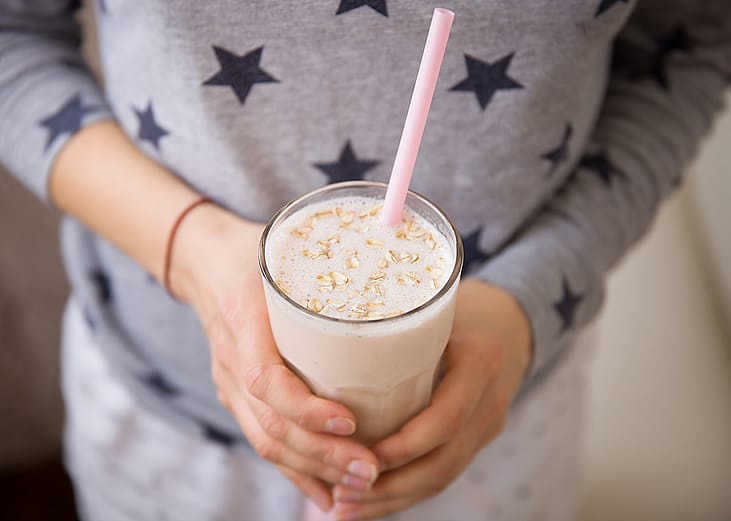 A woman holding a glass of blended oats drink. Oatzempic is one of the viral weight loss hack trends of the past year.
