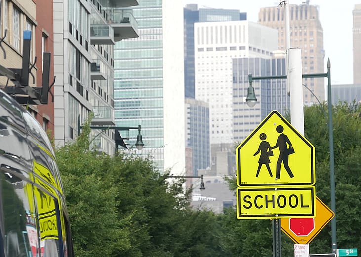 A yellow school zone sign for children's pedestrian crossing in a New York street.