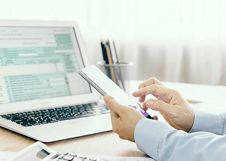 Businessman looking through phone and with a laptop is filling out a tax return form.