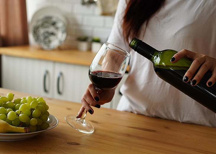 A woman pours a glass of red wine at home.