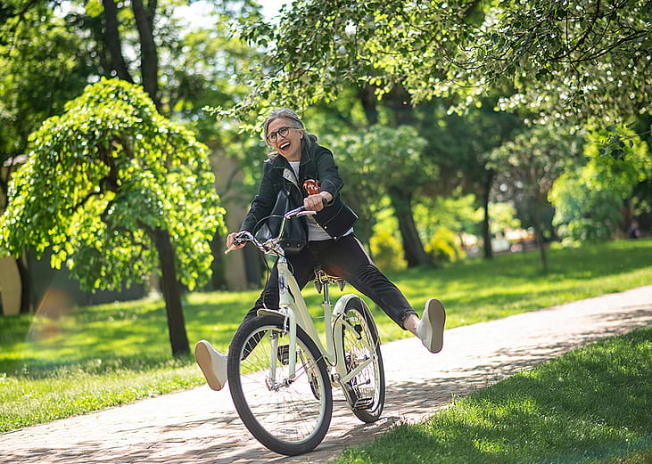 A middle aged woman happily having a stroll on a bike in a park.