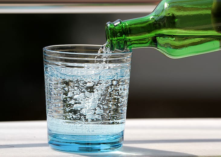 Sparkling water poured onto a glass from its bottle.